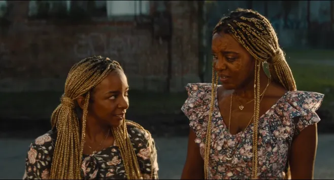 Two women with braided hairstyles standing together outdoors, wearing floral print dresses.