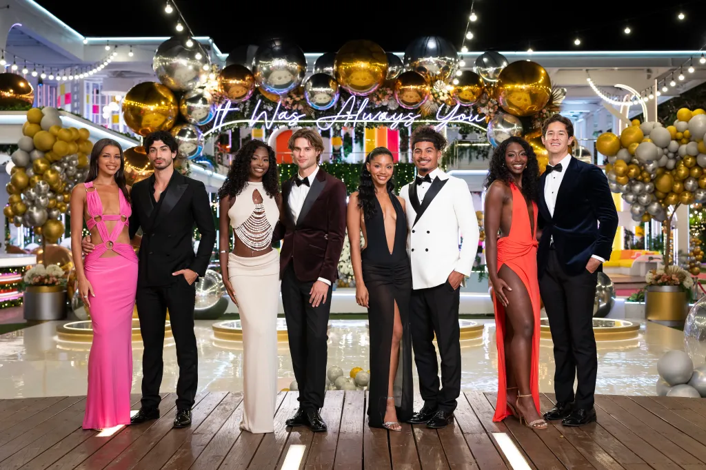 A group of well-dressed people posing in front of a festive backdrop with gold and silver balloons and the text "It was always you".